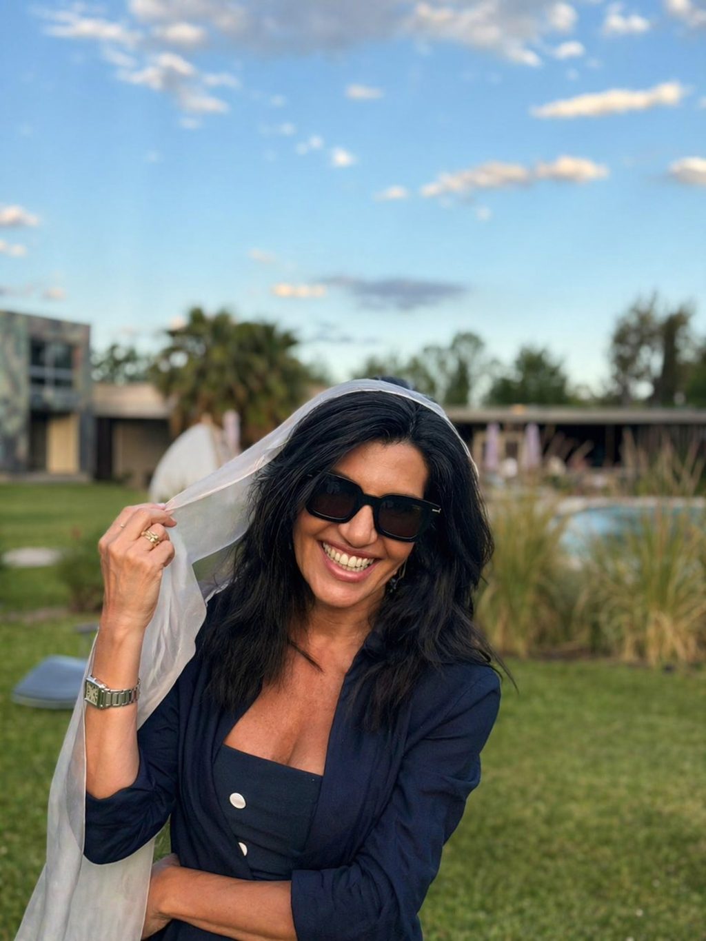 Angela Di Verbeno sorrindo ao ar livre, segurando um véu translúcido
